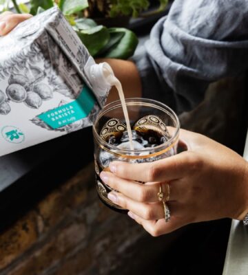 Photo shows someone pouring Milkadamia macadamia milk into a cup of coffee. The brand's new product is "2D printed" oat milk.