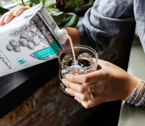 Photo shows someone pouring Milkadamia macadamia milk into a cup of coffee. The brand's new product is "2D printed" oat milk.