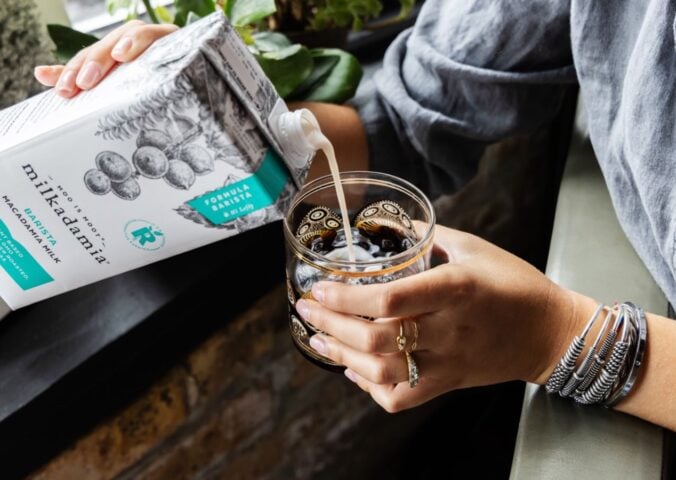 Photo shows someone pouring Milkadamia macadamia milk into a cup of coffee. The brand's new product is "2D printed" oat milk.