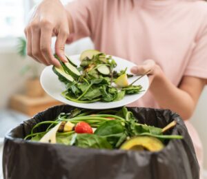 A woman throwing salad items and vegetables into a bin, contributing to food waste