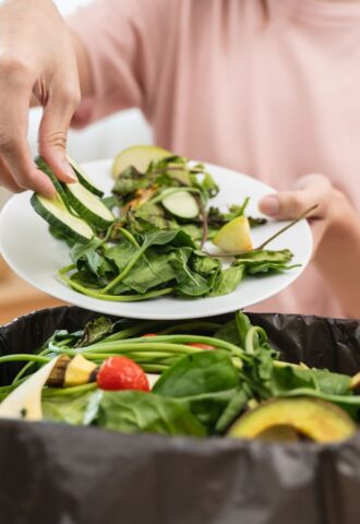 A woman throwing salad items and vegetables into a bin, contributing to food waste