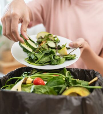 A woman throwing salad items and vegetables into a bin, contributing to food waste