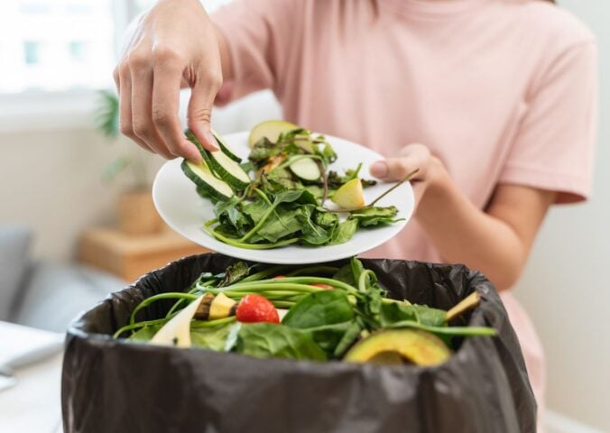 A woman throwing salad items and vegetables into a bin, contributing to food waste