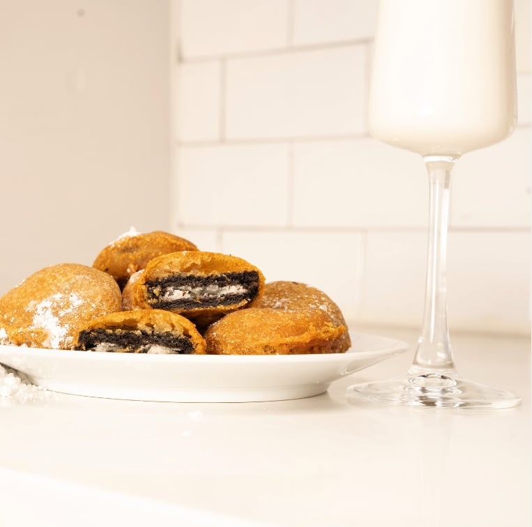 A selection of vegan fried Oreos next to a glass of milk in a champagne flute