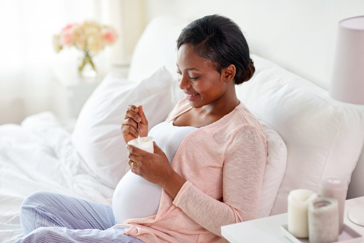 A pregnant woman eating vegan yogurt in bed