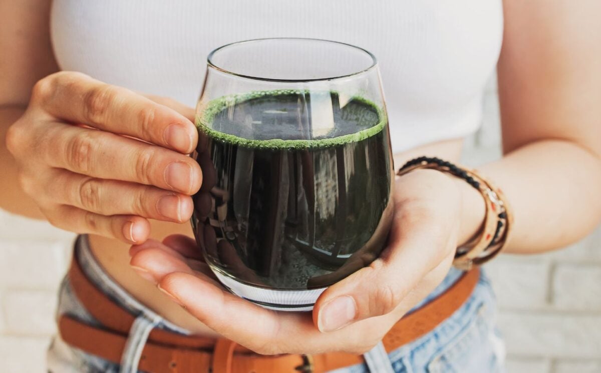 A woman holding a glass of dark green liquid containing cultivated spirulina, which is a good vegan source of B12