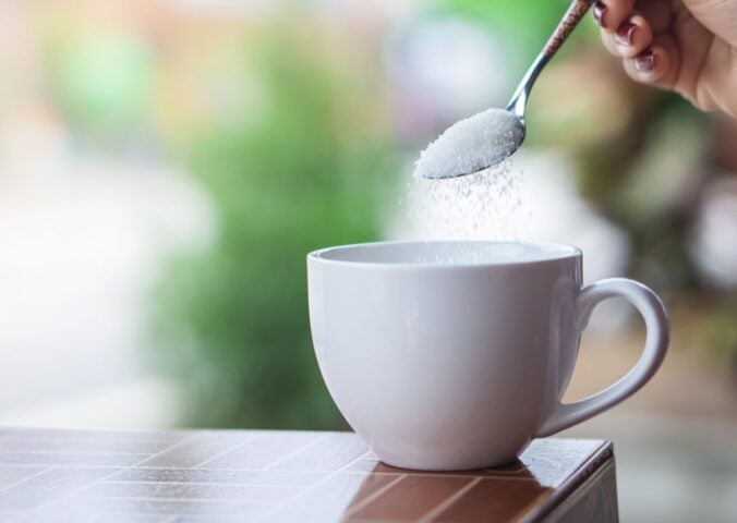 A person pouring sugar, which could be replaced in the future with sweet proteins, into a cup