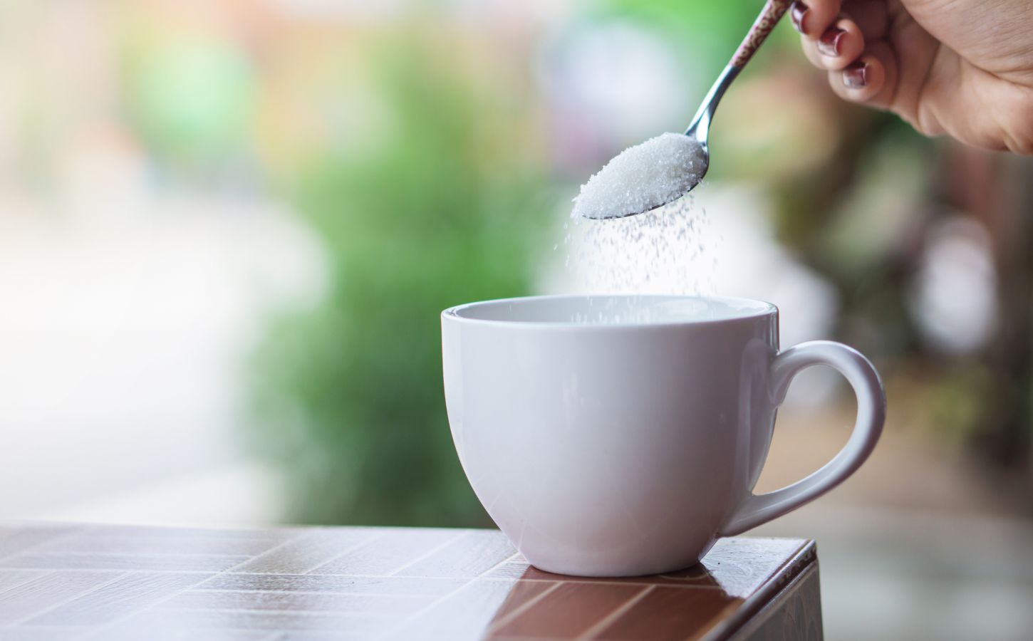 A person pouring sugar, which could be replaced in the future with sweet proteins, into a cup