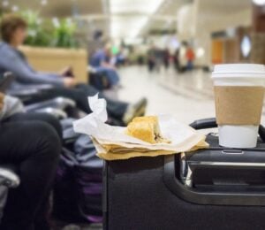 A vegan snack and a coffee in a takeaway cup balancing on a suitcase in a UK airport