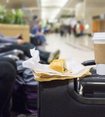 A vegan snack and a coffee in a takeaway cup balancing on a suitcase in a UK airport