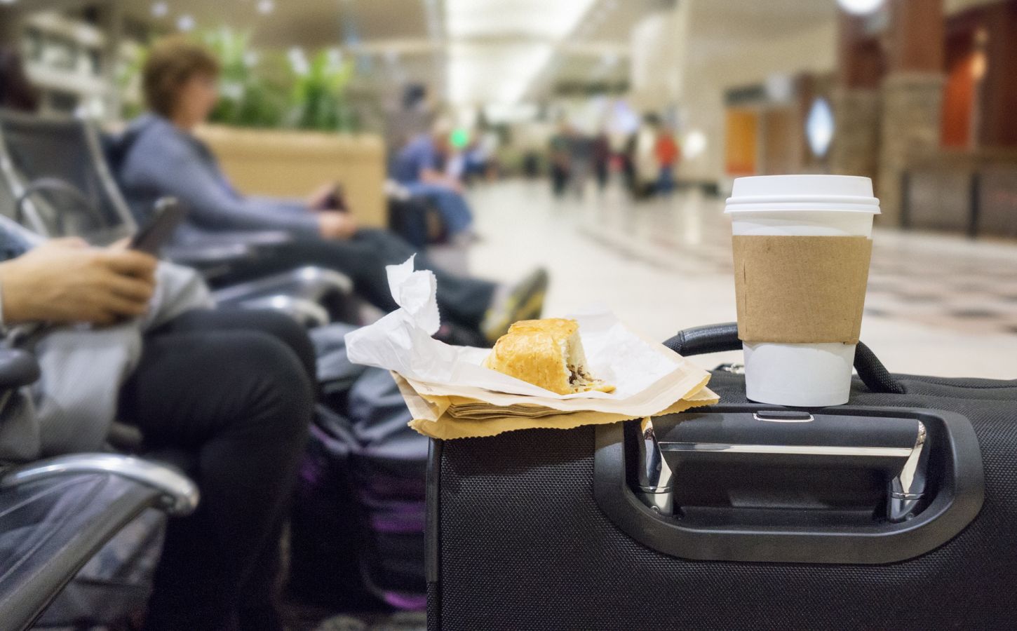 A vegan snack and a coffee in a takeaway cup balancing on a suitcase in a UK airport