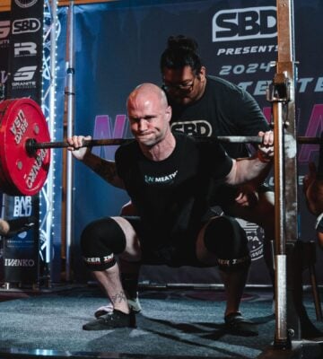 Photo shows Daniel Austin, aka the "Vegan Meathead" squatting during a powerlifting competition with the support of his team