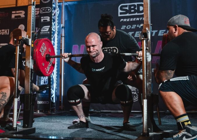 Photo shows Daniel Austin, aka the "Vegan Meathead" squatting during a powerlifting competition with the support of his team