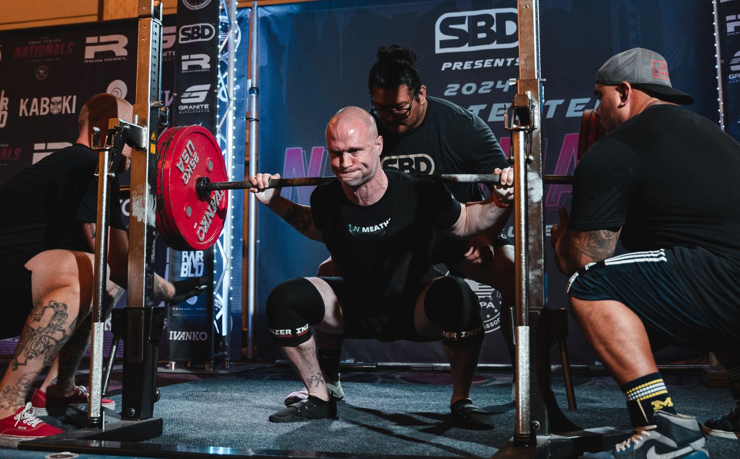 Photo shows Daniel Austin, aka the "Vegan Meathead" squatting during a powerlifting competition with the support of his team