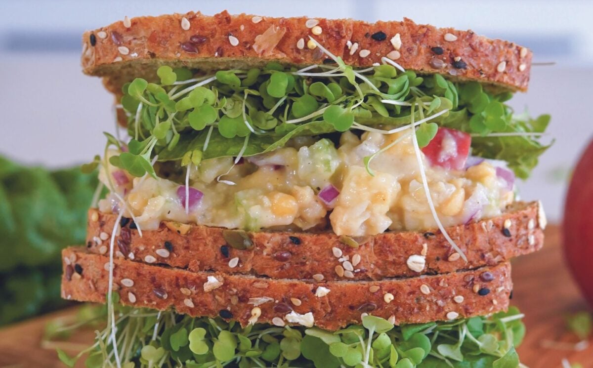 a vegan apple and chickpea salad sandwich with brown bread, lettuce, and sprouts great for vegan packed lunch