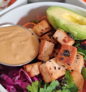 a picture of a vegan rice power bowl with peanut sauce, avocado, tofu, cucumber, bell pepper, brown rice