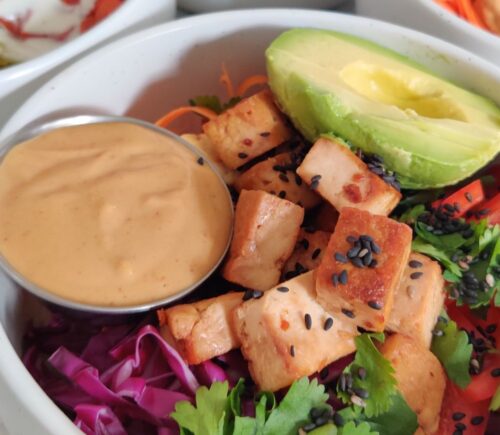 a picture of a vegan rice power bowl with peanut sauce, avocado, tofu, cucumber, bell pepper, brown rice