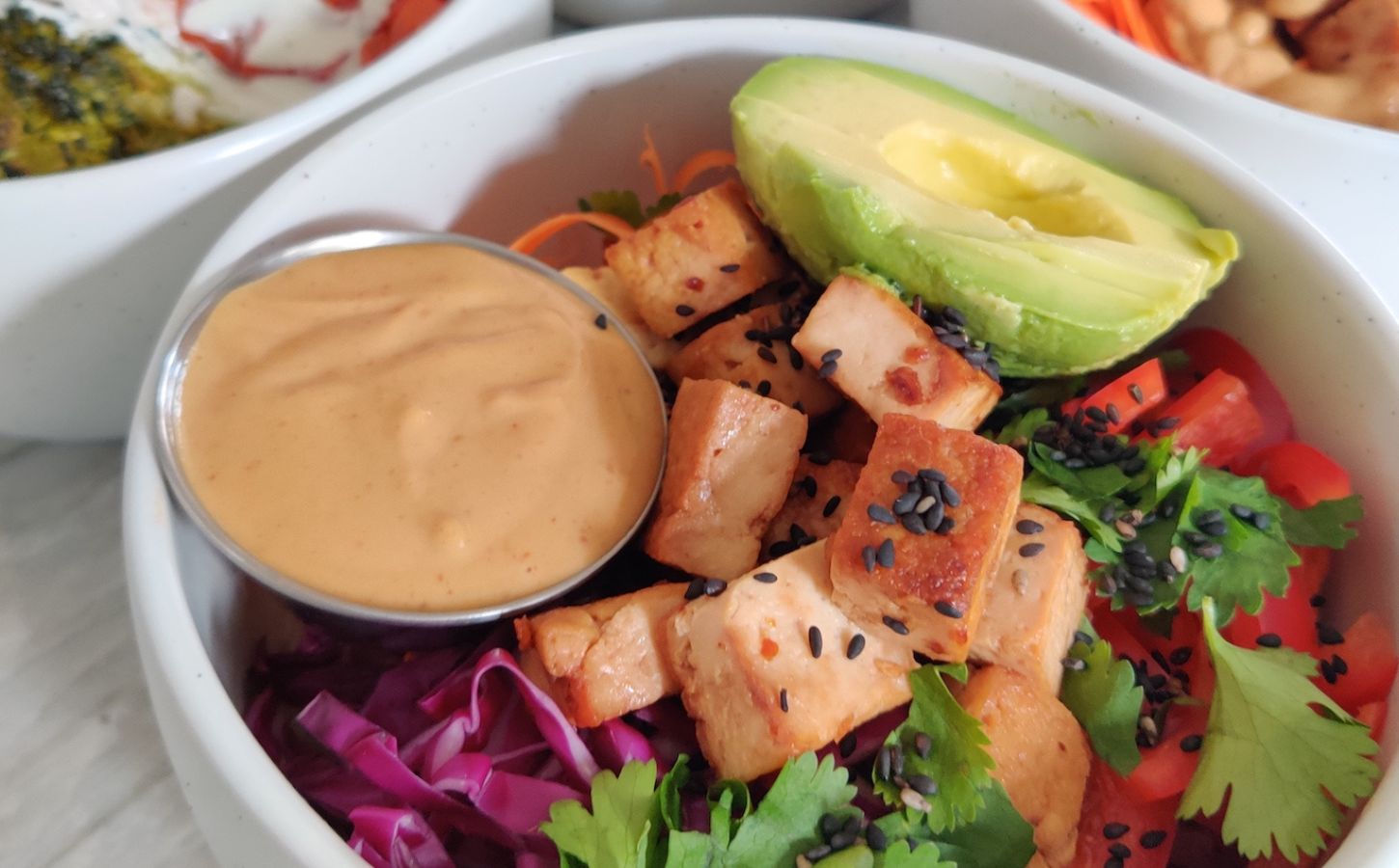 a picture of a vegan rice power bowl with peanut sauce, avocado, tofu, cucumber, bell pepper, brown rice