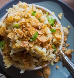 a picture of a cupful of au gratin hash brown casserole topped with cornflakes and scallion