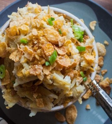 a picture of a cupful of au gratin hash brown casserole topped with cornflakes and scallion