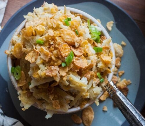 a picture of a cupful of au gratin hash brown casserole topped with cornflakes and scallion