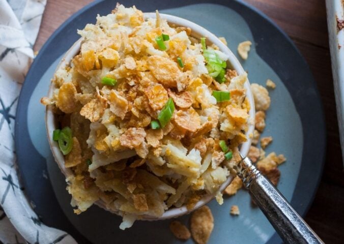 a picture of a cupful of au gratin hash brown casserole topped with cornflakes and scallion