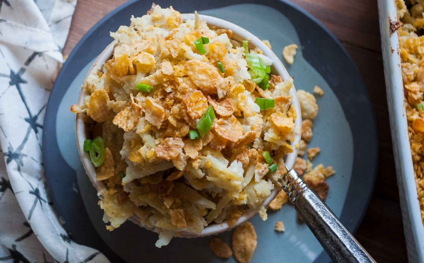 a picture of a cupful of au gratin hash brown casserole topped with cornflakes and scallion