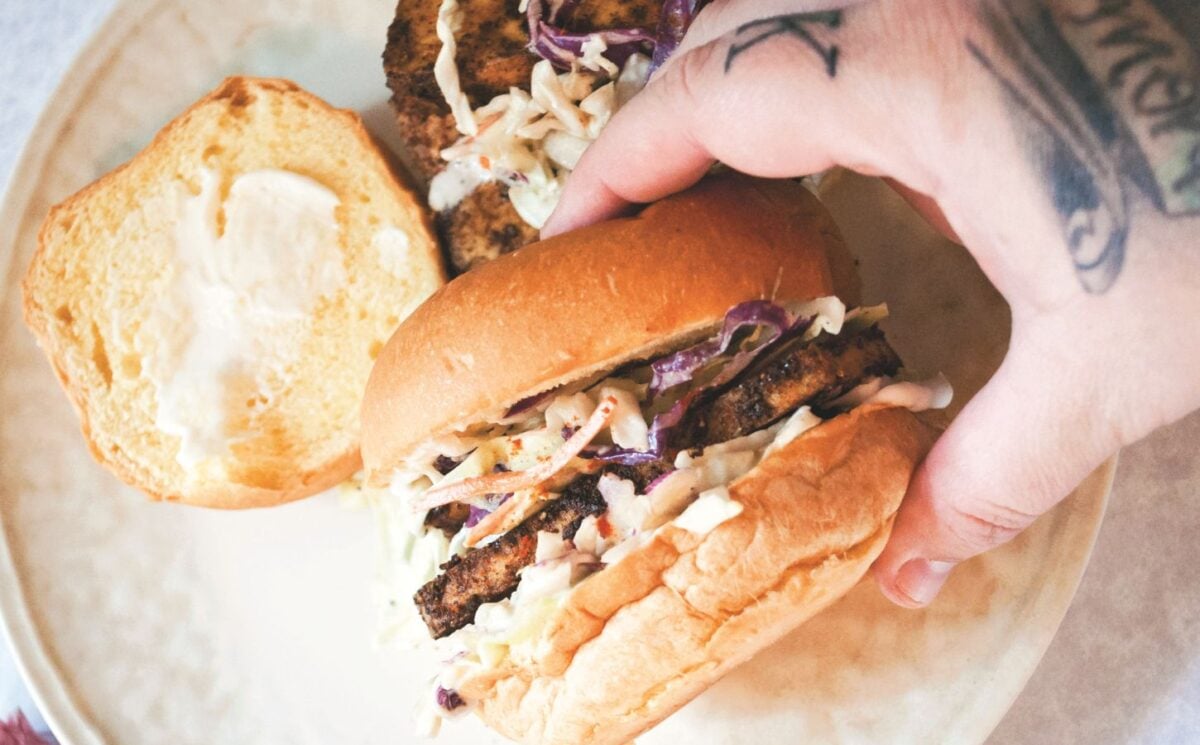 a picture of a hand holding a blackened tofu and coleslaw sandwich