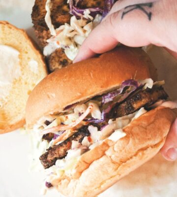 a picture of a hand holding a blackened tofu and coleslaw sandwich
