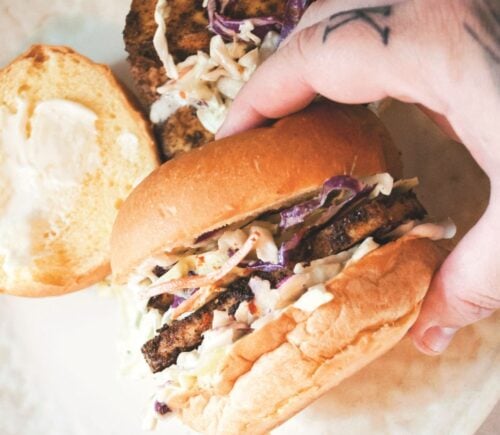 a picture of a hand holding a blackened tofu and coleslaw sandwich