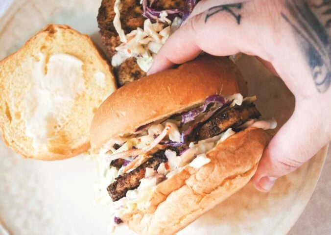 a picture of a hand holding a blackened tofu and coleslaw sandwich