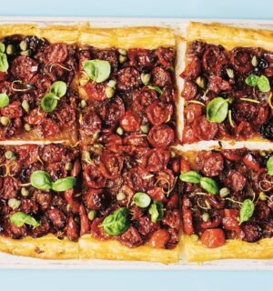 a picture of six squares of a caramelized shallot and tomato tart topped with basil and capers