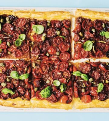 a picture of six squares of a caramelized shallot and tomato tart topped with basil and capers