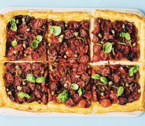 a picture of six squares of a caramelized shallot and tomato tart topped with basil and capers