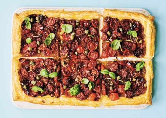 a picture of six squares of a caramelized shallot and tomato tart topped with basil and capers