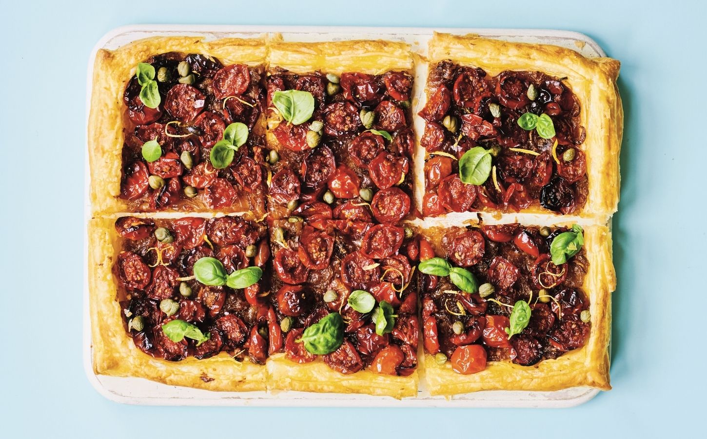 a picture of six squares of a caramelized shallot and tomato tart topped with basil and capers