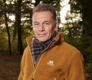 Photo shows Chris Packham standing in a woodland clearing