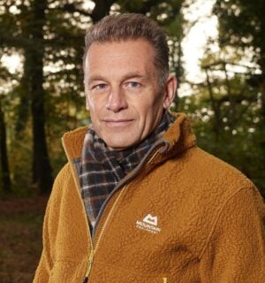 Photo shows Chris Packham standing in a woodland clearing