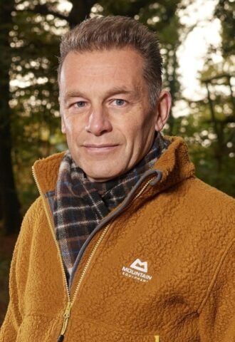 Photo shows Chris Packham standing in a woodland clearing