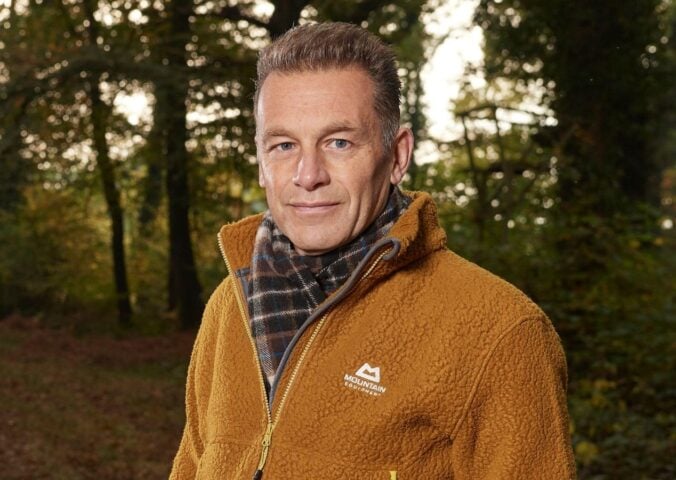 Photo shows Chris Packham standing in a woodland clearing