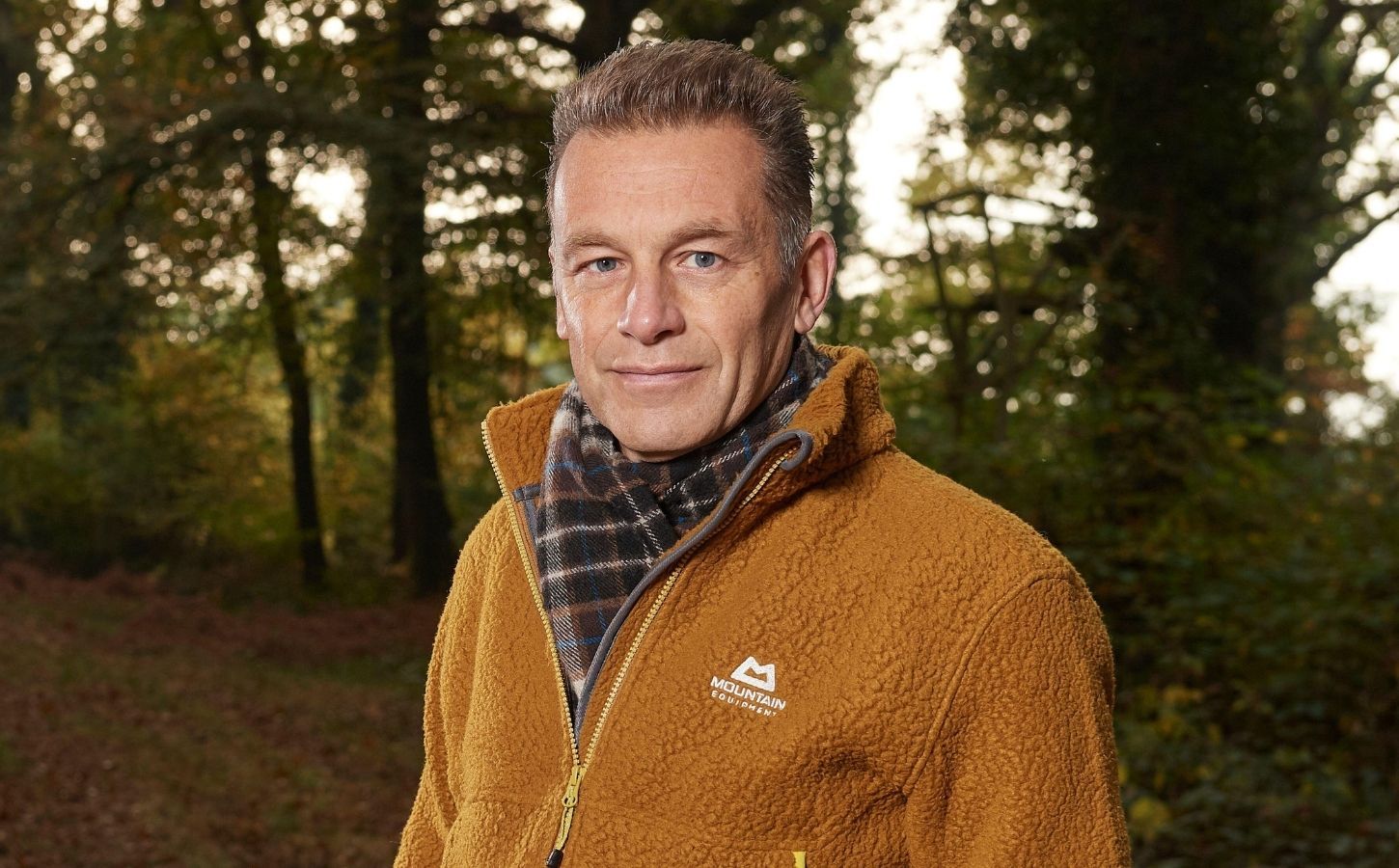 Photo shows Chris Packham standing in a woodland clearing