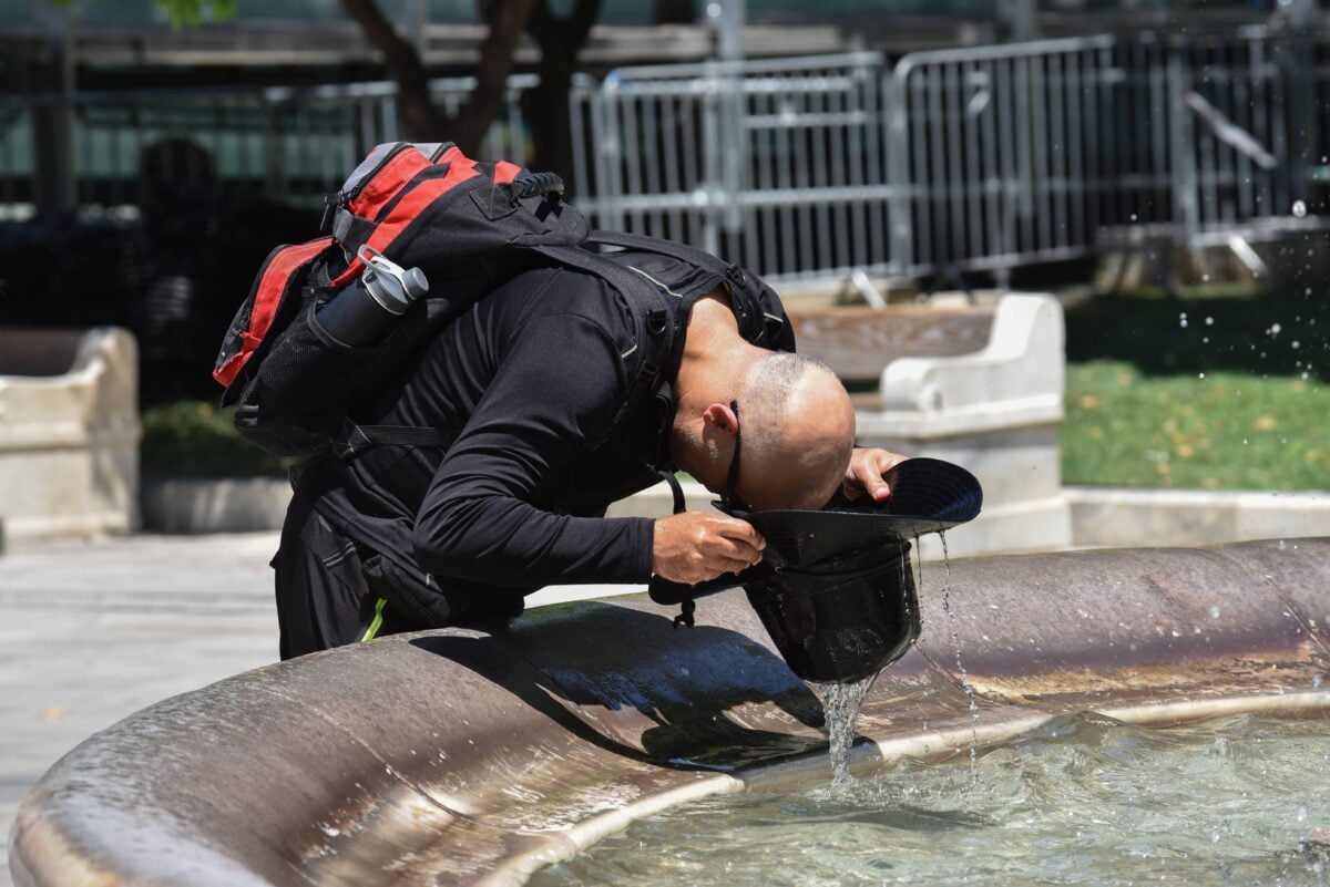 A man filling his hat with water from a fountain and pouring it on his head in the middle of a heatwave in Greece