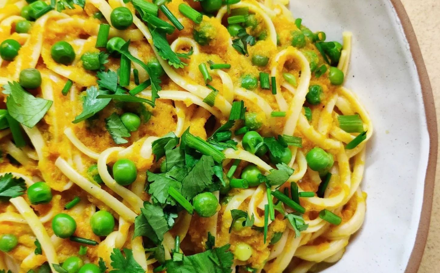 a picture of a curried carrot pasta topped with peas and cilantro