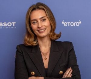 Ella Woodward, owner of Deliciously Ella, in a black suit in front of a purple background