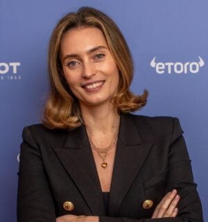 Ella Woodward, owner of Deliciously Ella, in a black suit in front of a purple background