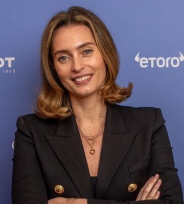 Ella Woodward, owner of Deliciously Ella, in a black suit in front of a purple background