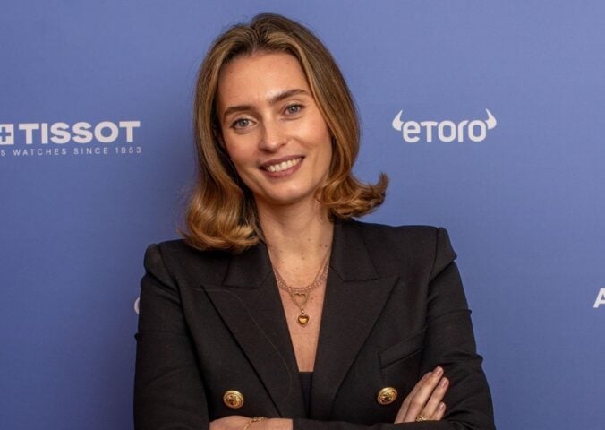 Ella Woodward, owner of Deliciously Ella, in a black suit in front of a purple background