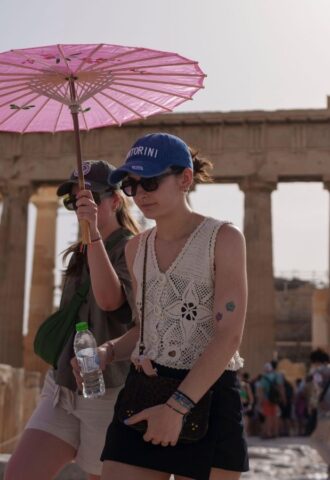 Two people walking by the Acropolis in Athens during a heatwave carrying a pink umbrella