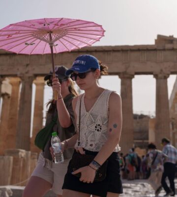 Two people walking by the Acropolis in Athens during a heatwave carrying a pink umbrella