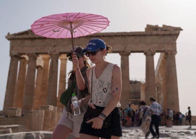 Two people walking by the Acropolis in Athens during a heatwave carrying a pink umbrella